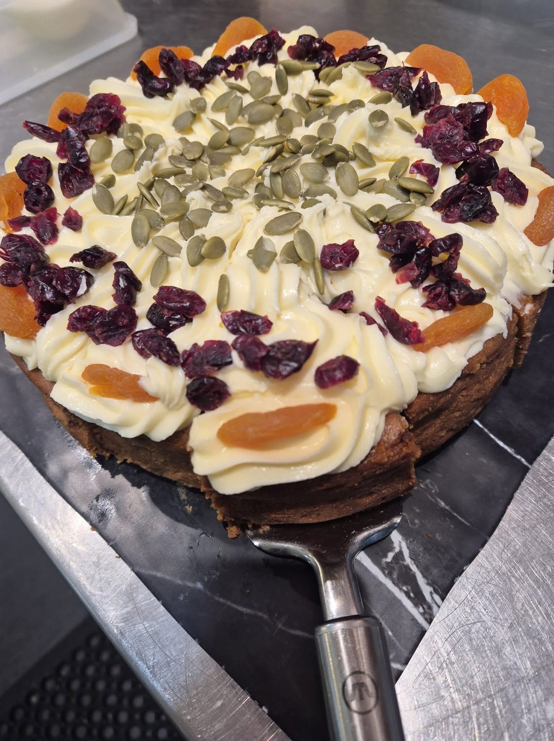 Carrot cake topped with cream cheese icing, pepitas and cranberries